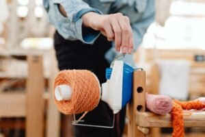 Person winding orange yarn on a spool in a creative craft studio. Warm atmosphere.