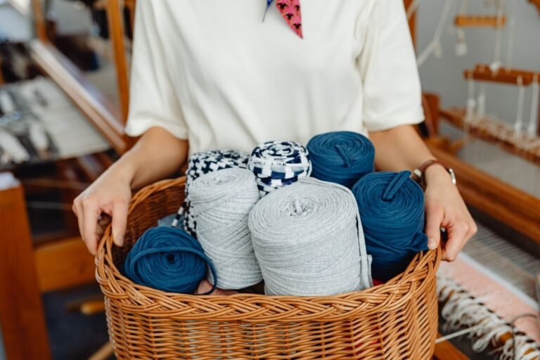 A person holds a wicker basket filled with colorful yarn spools in a weaving workshop.